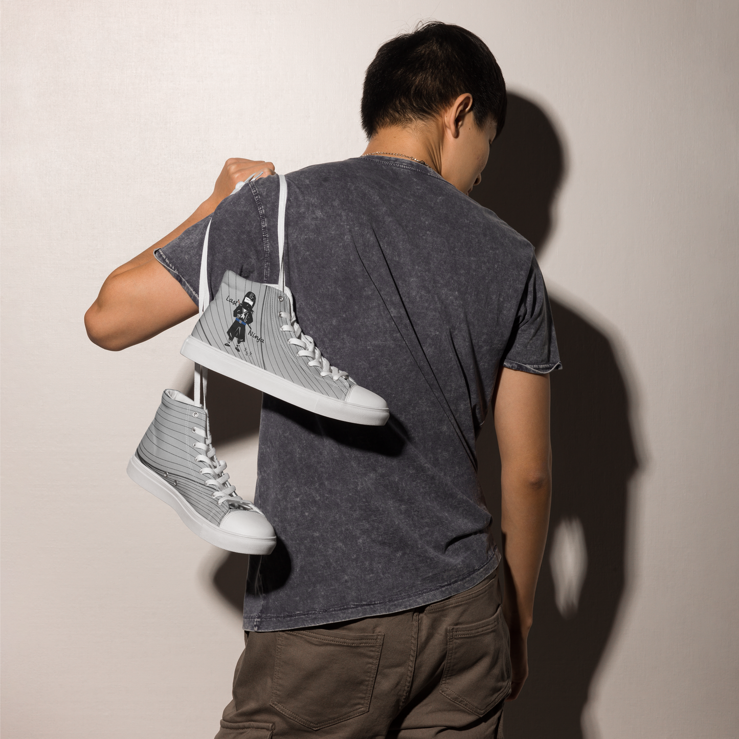 Person holding a pair of gray high-top sneakers with a ninja graphic design against a plain background
