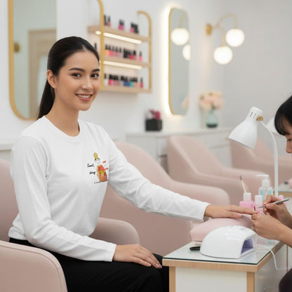 Nail technician applying nail polish to a female client wearing a white sweatshirt with a playful Thai lady graphic and text "fun wear code" in a salon setting.