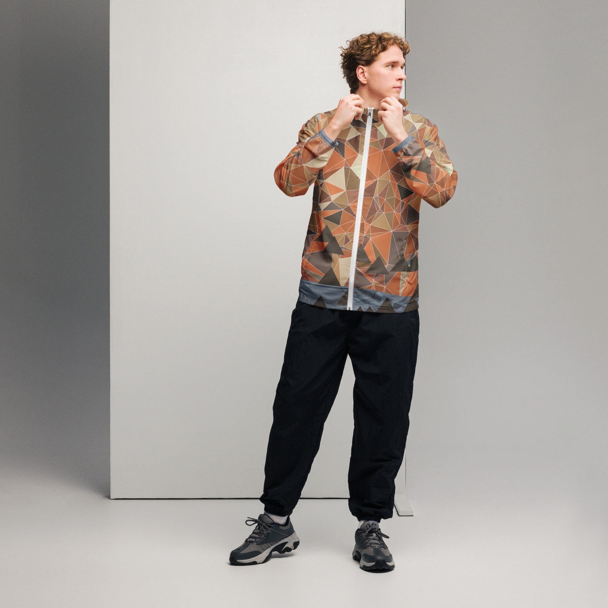 Person wearing a multicolor geometric patterned windbreaker jacket and black pants against a gray background