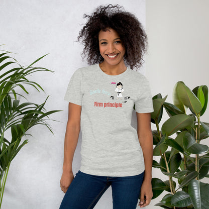 Woman wearing a gray t-shirt with text and judo graphics, standing between two plants against a white wall.